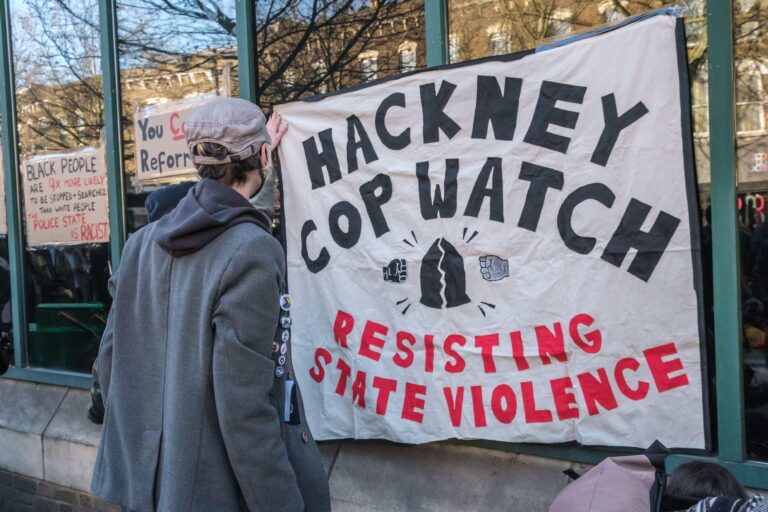 London, UK. 18th Mar 2022. The Hackney Cop Watch banner is taped to the windows of Stoke Newington Police Station. After a few speeches their protestmoved to block the road and contine there road demanding no more police in schools after reports that 15 y